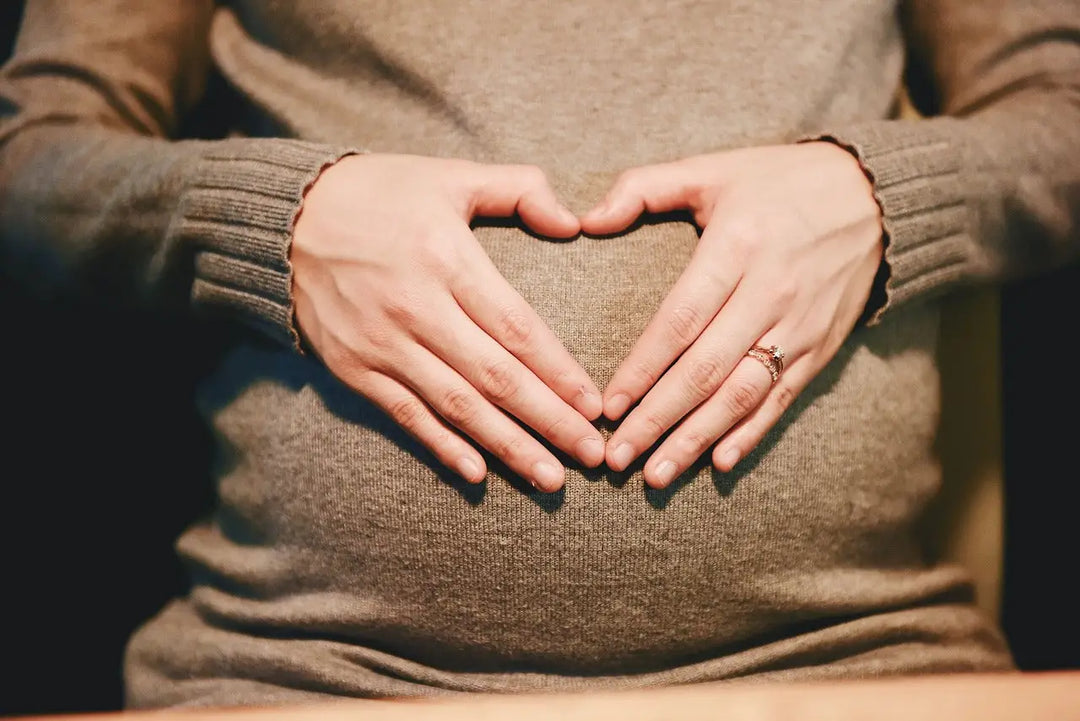 Eine schwangere Frau macht mit ihren Händen ein Herz auf dem Bauch